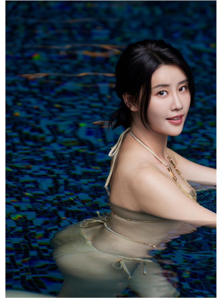 一位女性穿著泳衣，坐在藍色泳池中，微笑著望向鏡頭，背景是波光粼粼的水面。