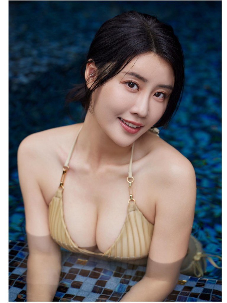 一位女性在游泳池中微笑，穿著淺色比基尼，上面有褶皺設計，背景是藍色的馬賽克瓷磚。