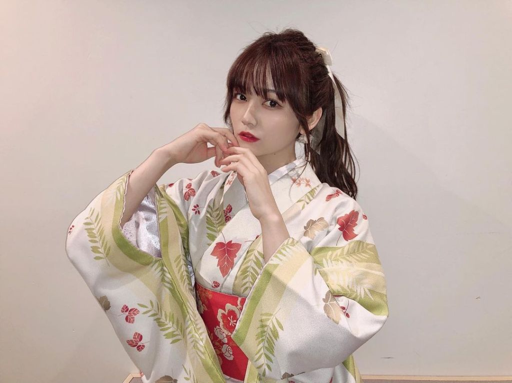 穿著華麗和服的女性，手指輕放在臉頰上，背景淺色牆壁