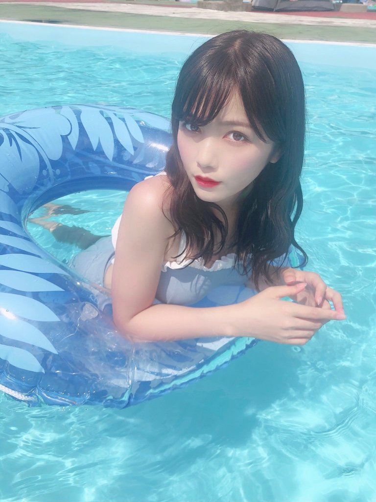 一位女孩坐在清澈的泳池中，穿著水著，手抱著藍色浮圈，淺笑著望向鏡頭。
