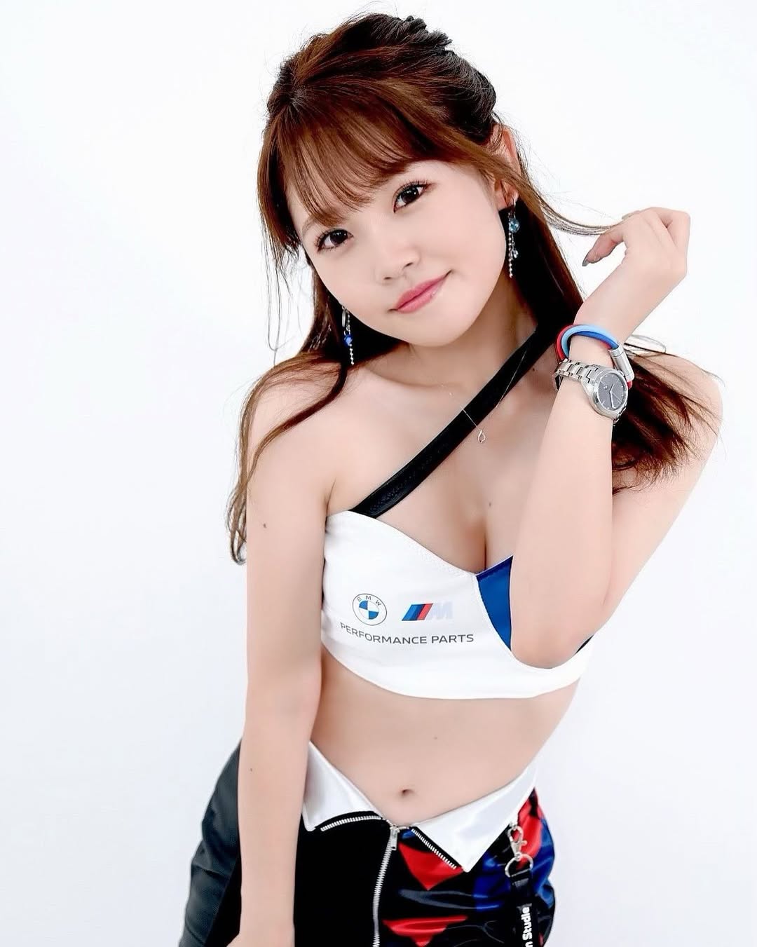 一位穿著BMW性能部件運動服的年輕女性在白色背景前微笑，手撫弄頭髮。