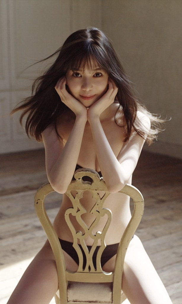 一名女性坐在一把金色靠背椅上，雙手托著臉，面帶微笑，背景為柔和的室內光線。