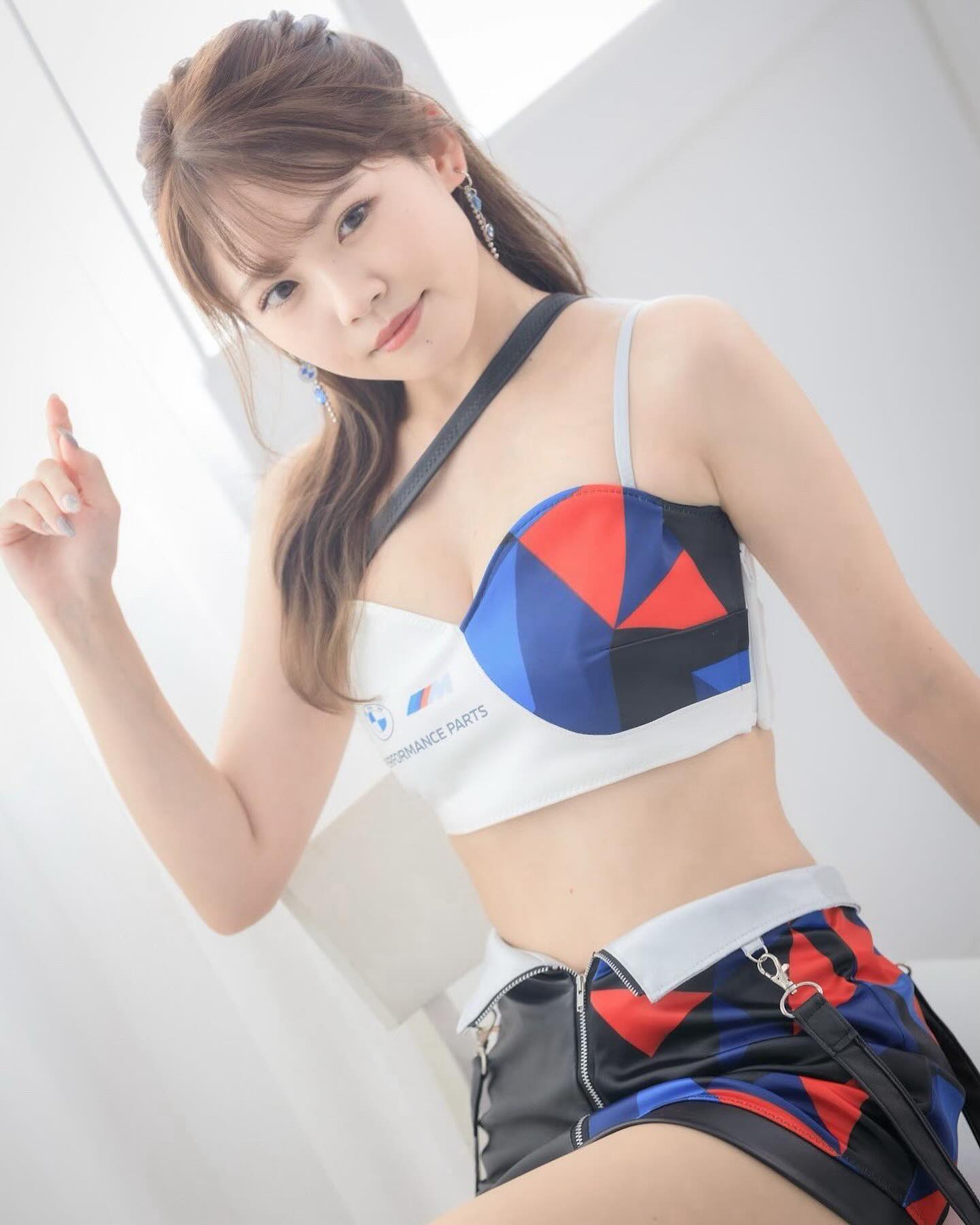 一位女性模特兒穿著色彩鮮豔的兩件式服裝，擺出微笑姿勢，背景為簡約的白色室內環境。