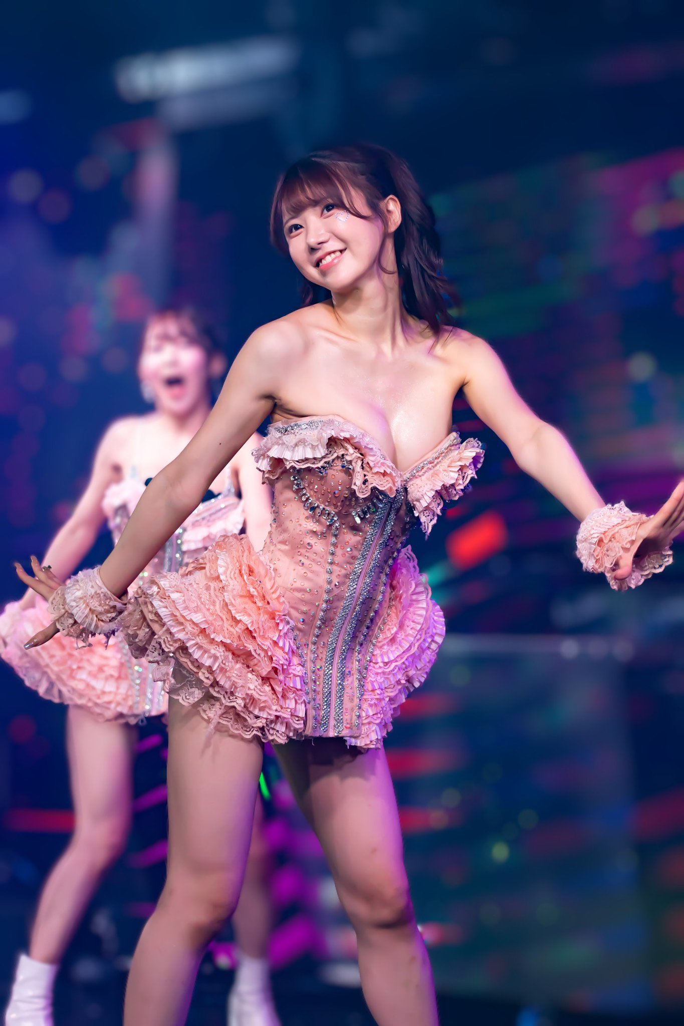 一位穿著粉色舞衣的女舞者在舞台上表演，展現出愉快的笑容，背景有彩色燈光效果。