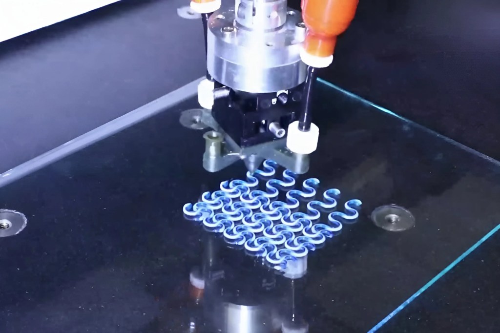 一個精密的3D打印機正在玻璃板上打印藍色波浪形狀的圖案。