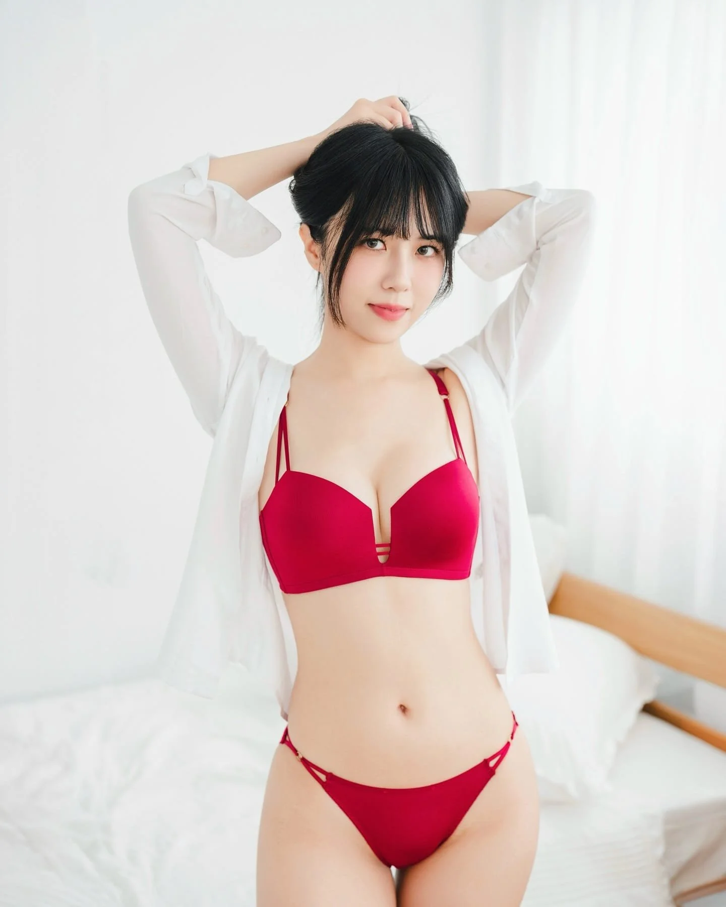 穿著紅色泳衣和白色襯衫的女性，正在以自然的姿勢在明亮的室內環境中擺姿勢。