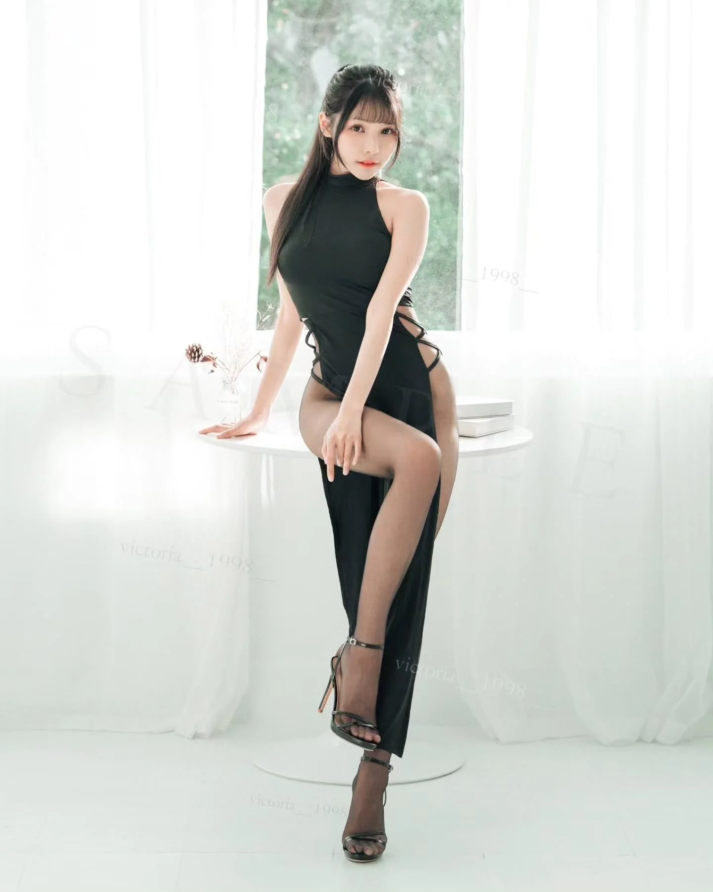 一位女性身穿黑色連身裙，坐在窗邊，周圍有亮麗的自然光，展現出優雅的姿態和長腿。