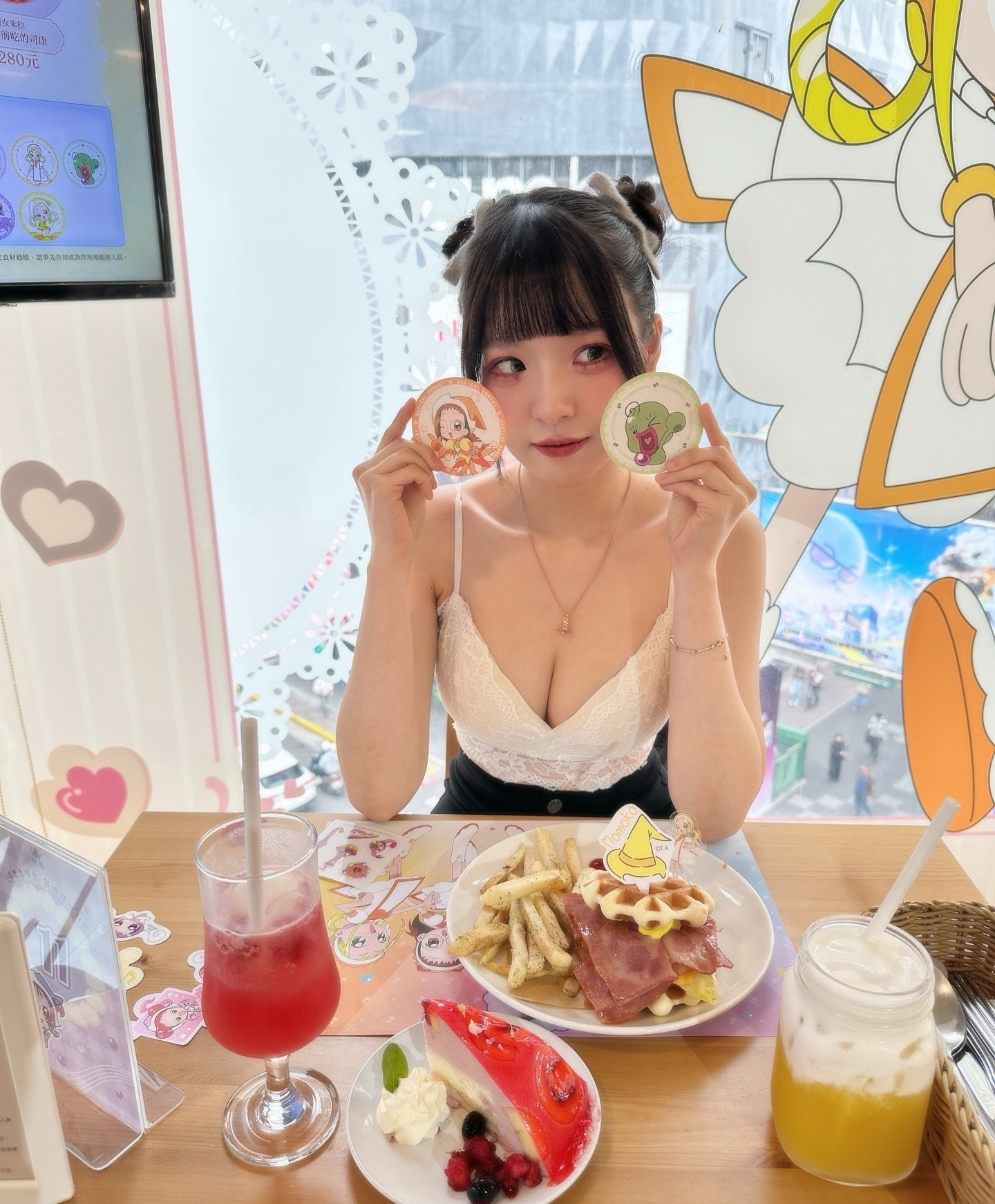 一名女性坐在餐桌前，手持兩個印有卡通角色的圓形餅乾，桌子上擺有彩色飲品和美食，包括薯條、早餐拼盤和蛋糕，背景有可愛的卡通裝飾。