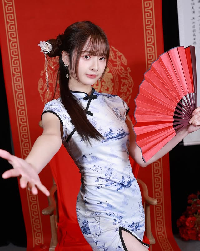 身穿中式旗袍的女性手持扇子，背景為紅色裝飾，展示出傳統文化氛圍。