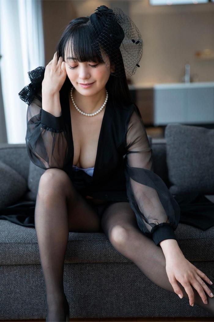 一位女性坐在沙發上，穿著黑色透明服裝，配戴珍珠項鍊，正低頭思考，背景為柔和的室內環境。