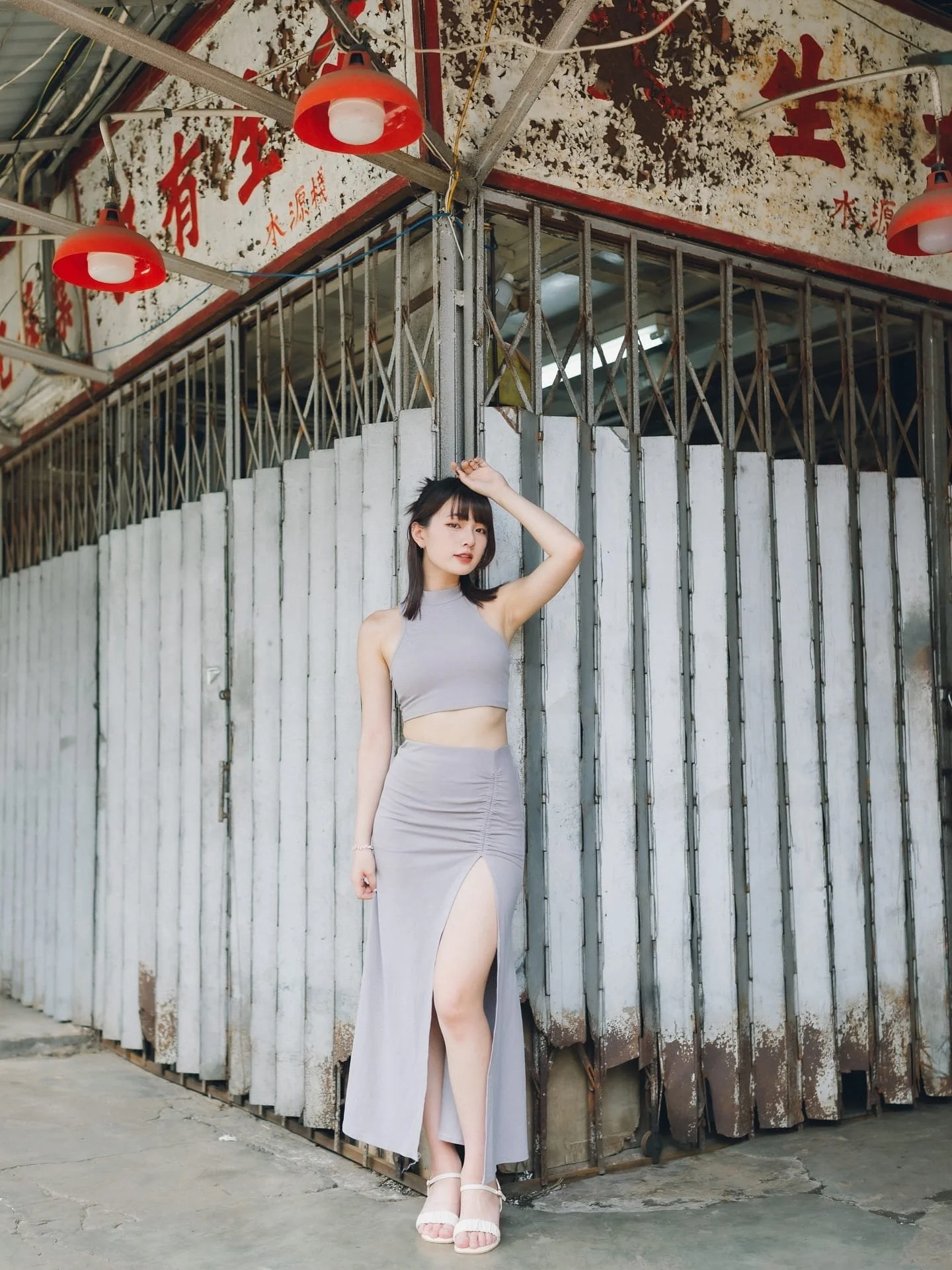 一位穿著淺灰色兩件式服裝的女性，站在帶有復古風格的背景前，表情自信。
